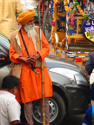 Man in an orange turban leans on a car in the street in Delhi