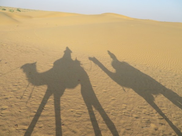 Shadows of camels and riders on sand dunes