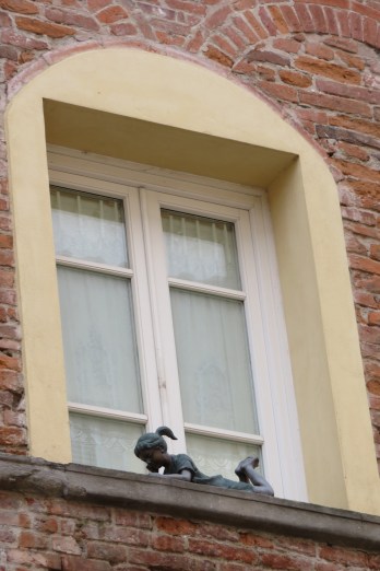 A sculpture of a little girl reading book on a window sill in Lucca Italy