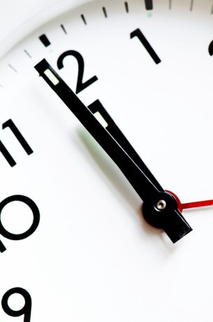 A white clock with black numbers and hands strikes 12