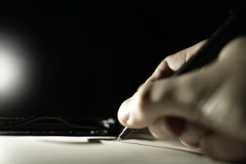 Black and white photo of a hand holding a pen and writing on paper